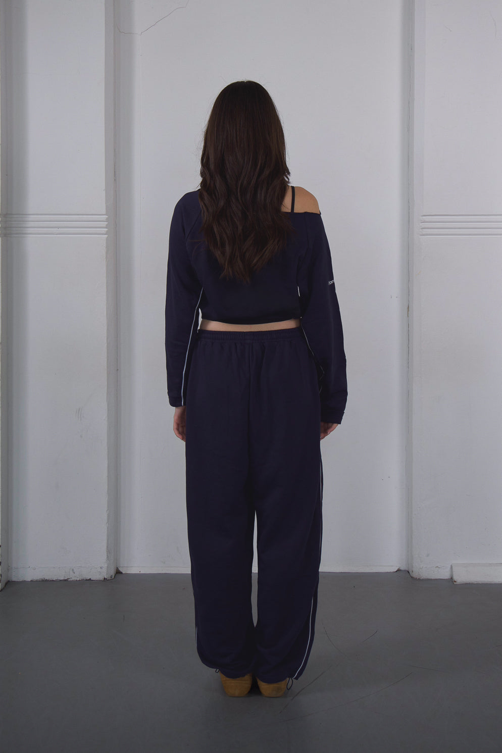 Person wearing a navy blue outfit standing against a white wall.