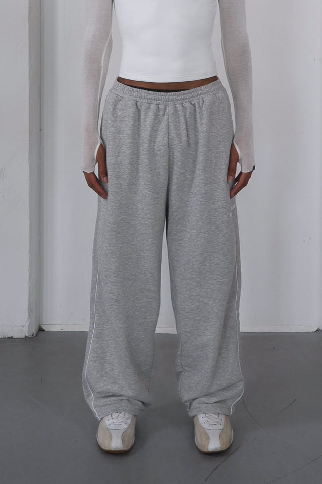 Person wearing a white top and gray pants against a plain white background