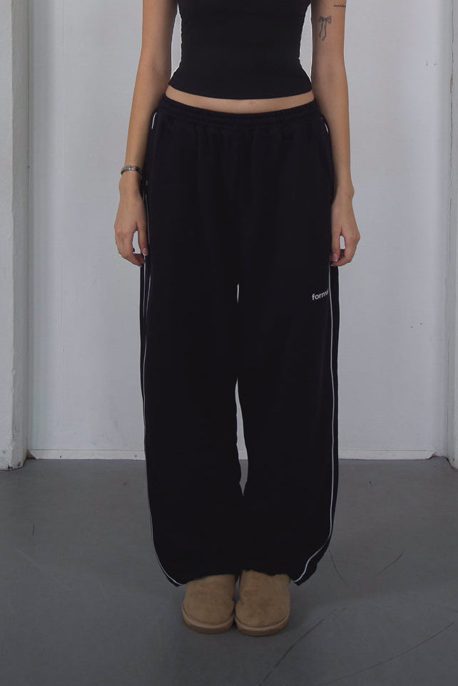 Person wearing black pants with white stripes and a black top against a plain background