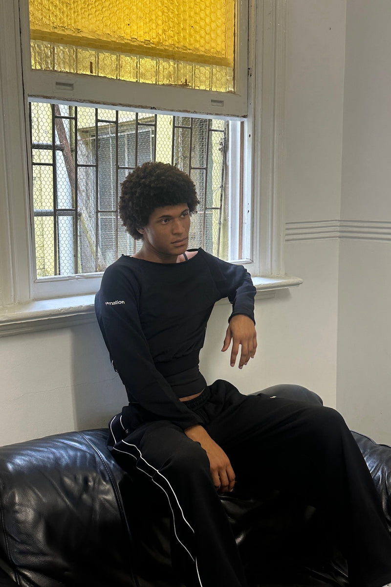 Person sitting on a couch in a room with a window in the background. Wearing black sweatset.