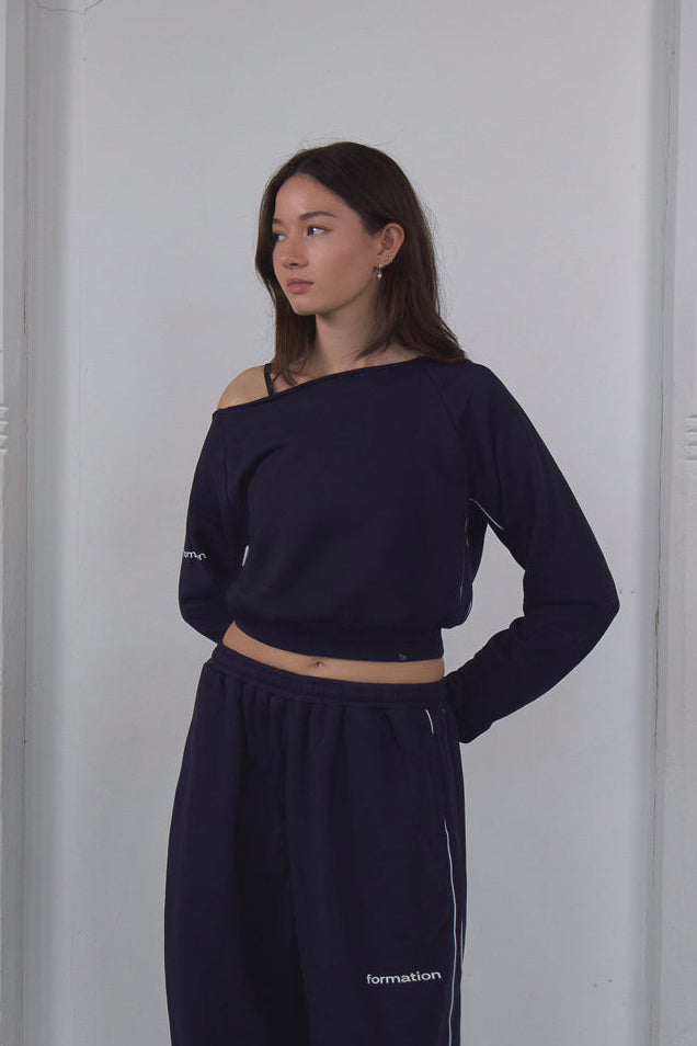Woman wearing a navy blue outfit with a white wall background