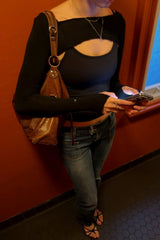 Person wearing a black top and blue jeans, holding a brown leather bag against a red wall.