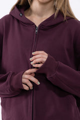 A close-up of a person wearing a deep plum purple zip-up hoodie, showing the front zipper, ribbed cuffs, and hands with light green nail polish.