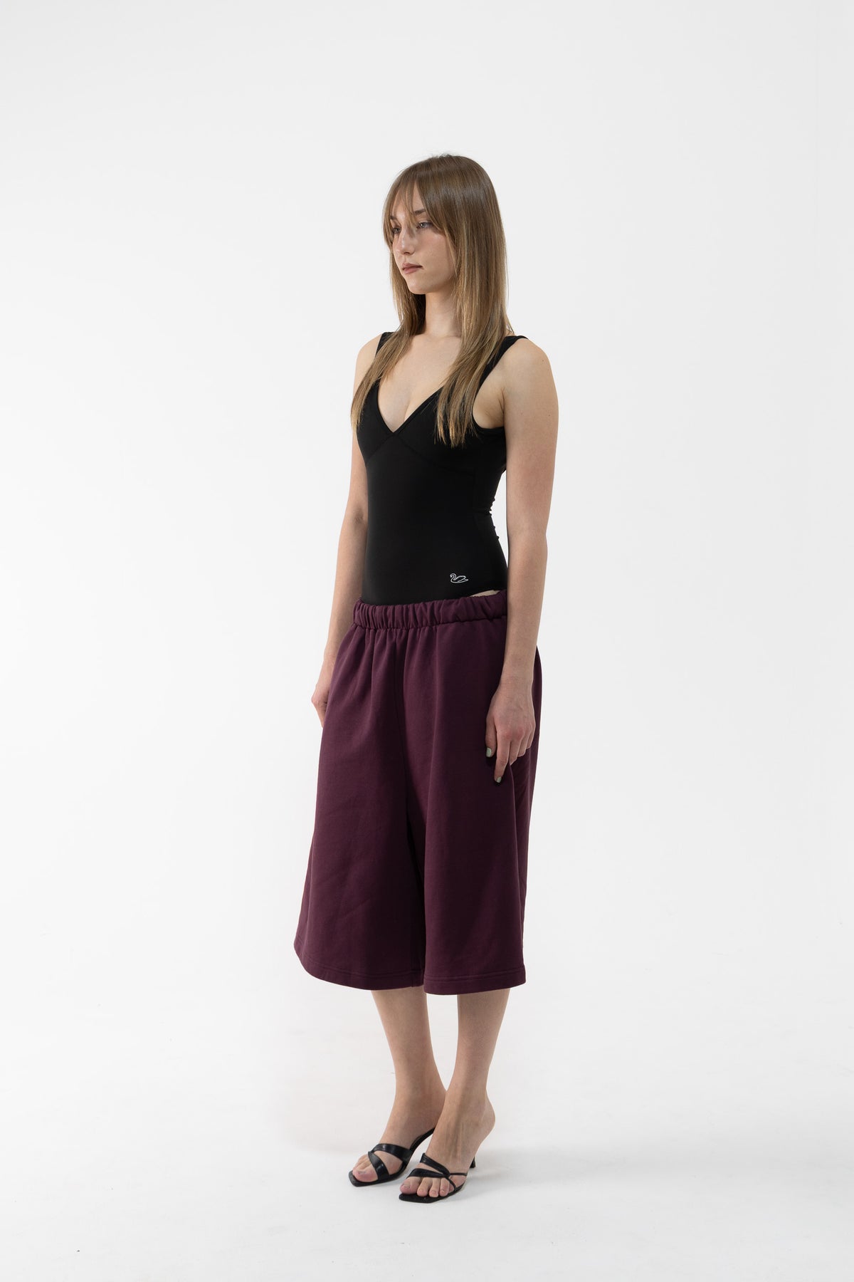 A dancer modeling a black sleeveless top and plum wide-leg cropped pants against a plain white studio background.