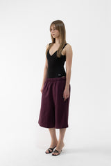 A dancer modeling a black sleeveless top and plum wide-leg cropped pants against a plain white studio background.