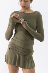 A dancer wearing an olive green long-sleeve ruched top and mini skirt with a boat neckline, shown from the head down against a plain white background.