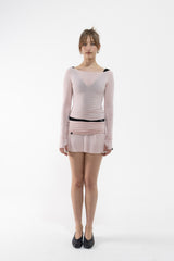 A dancer stands against a white studio background wearing a pale pink long-sleeve mini dress with black trim at the neckline and waist, paired with black flats.