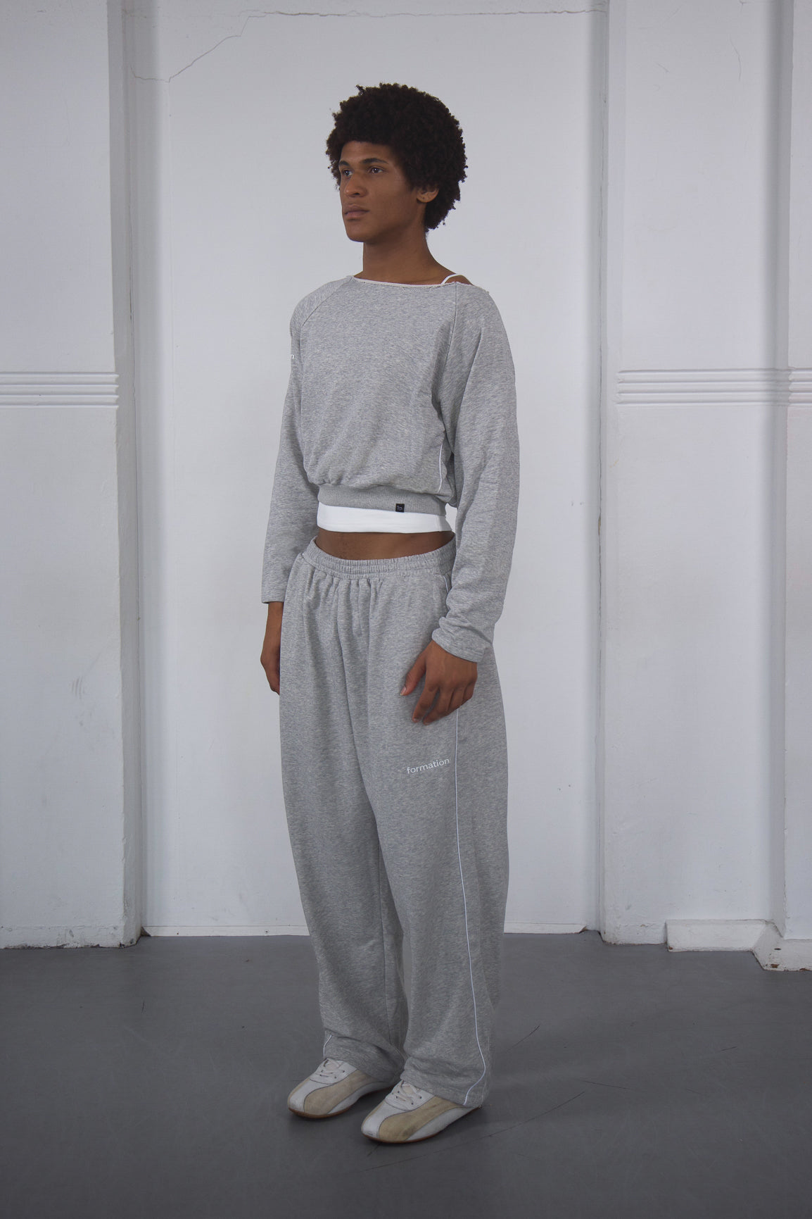 Person wearing a gray outfit standing against a white wall.