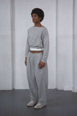 Person wearing a gray outfit standing against a white wall.