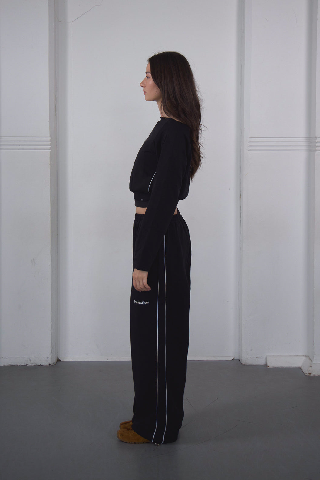 Woman wearing a black outfit with white stripes standing against a white wall.