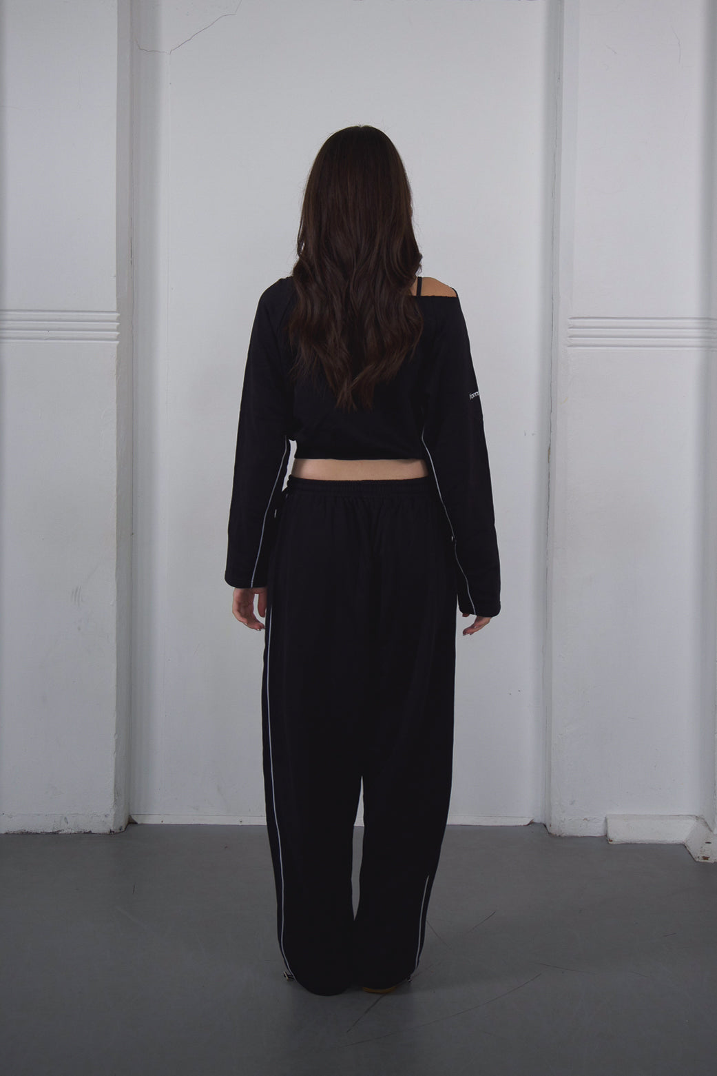 Person wearing a black outfit with a white wall background