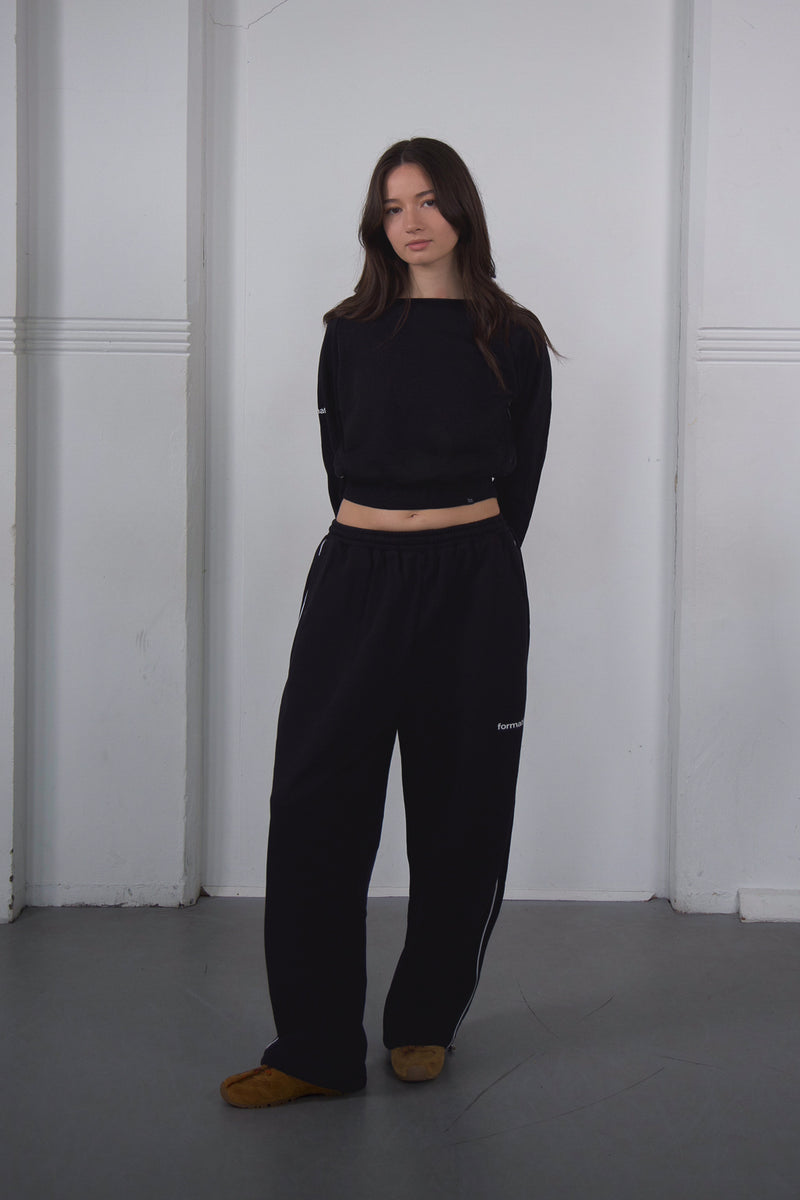 Person wearing a black outfit standing against a white wall.