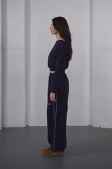 Woman wearing a navy blue outfit standing against a plain white wall.