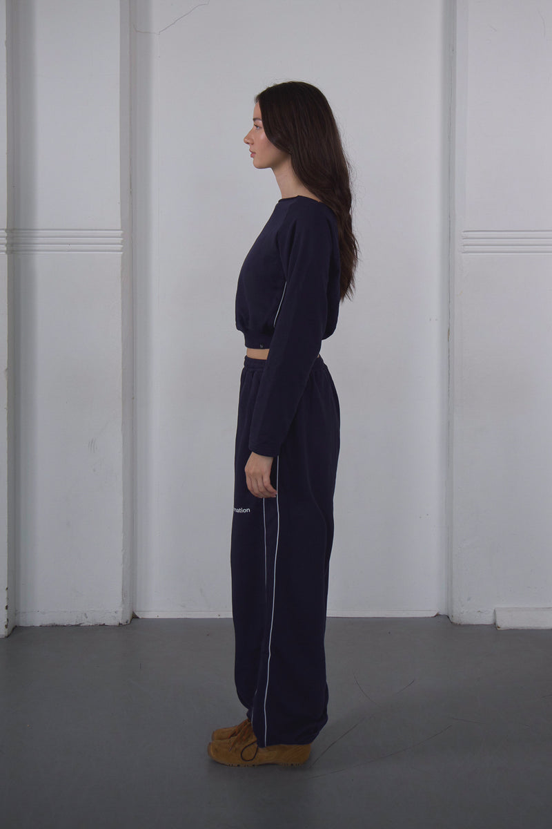 Woman wearing a navy blue outfit standing against a plain white wall.