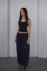Woman wearing a black crop top and navy pants against a white wall.