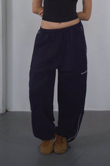 Woman wearing a black crop top and navy pants against a white wall.