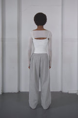 Person wearing a white top and grey pants against a white wall.