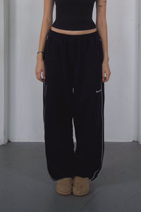 Person wearing black pants with white stripes and a black top against a plain background