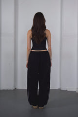 Person wearing a black outfit with wide-leg pants against a white wall.