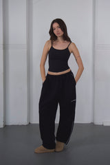 Woman wearing a black tank top and black pants standing against a white wall.