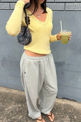 Person wearing a yellow top and gray sweatpants holding a drink against a gray wall.