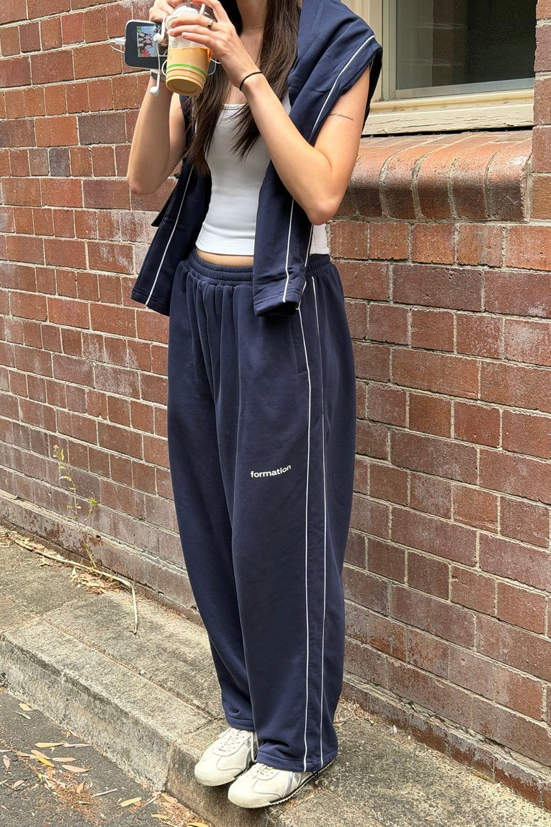 Person wearing navy tracksuit with white stripes against a brick wall.
