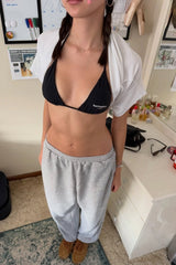 Person wearing a black 'formation' bikini top and gray sweatpants in a room.