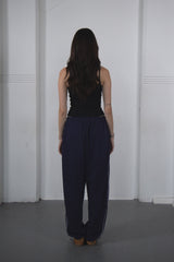 Person wearing a black sleeveless top and navy pants against a white wall.