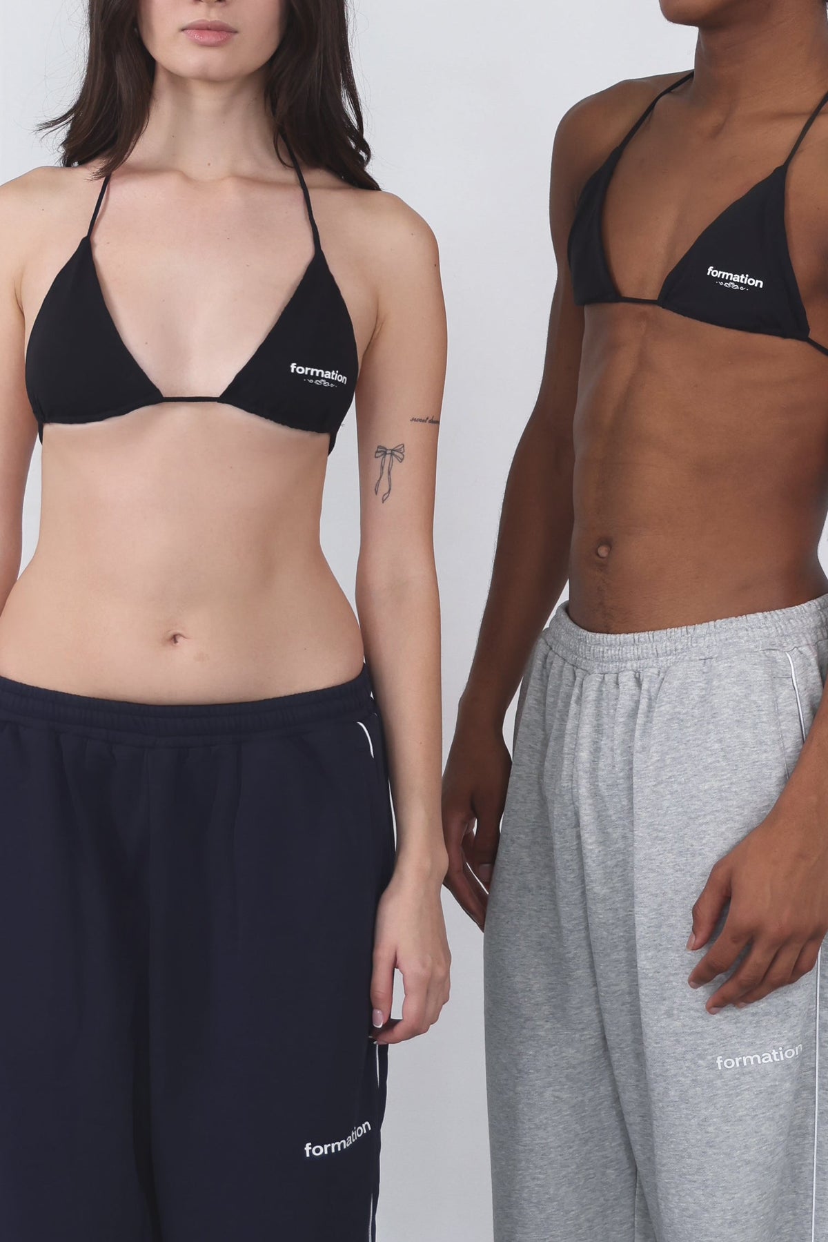 Two people wearing black triangle bras against a white background
