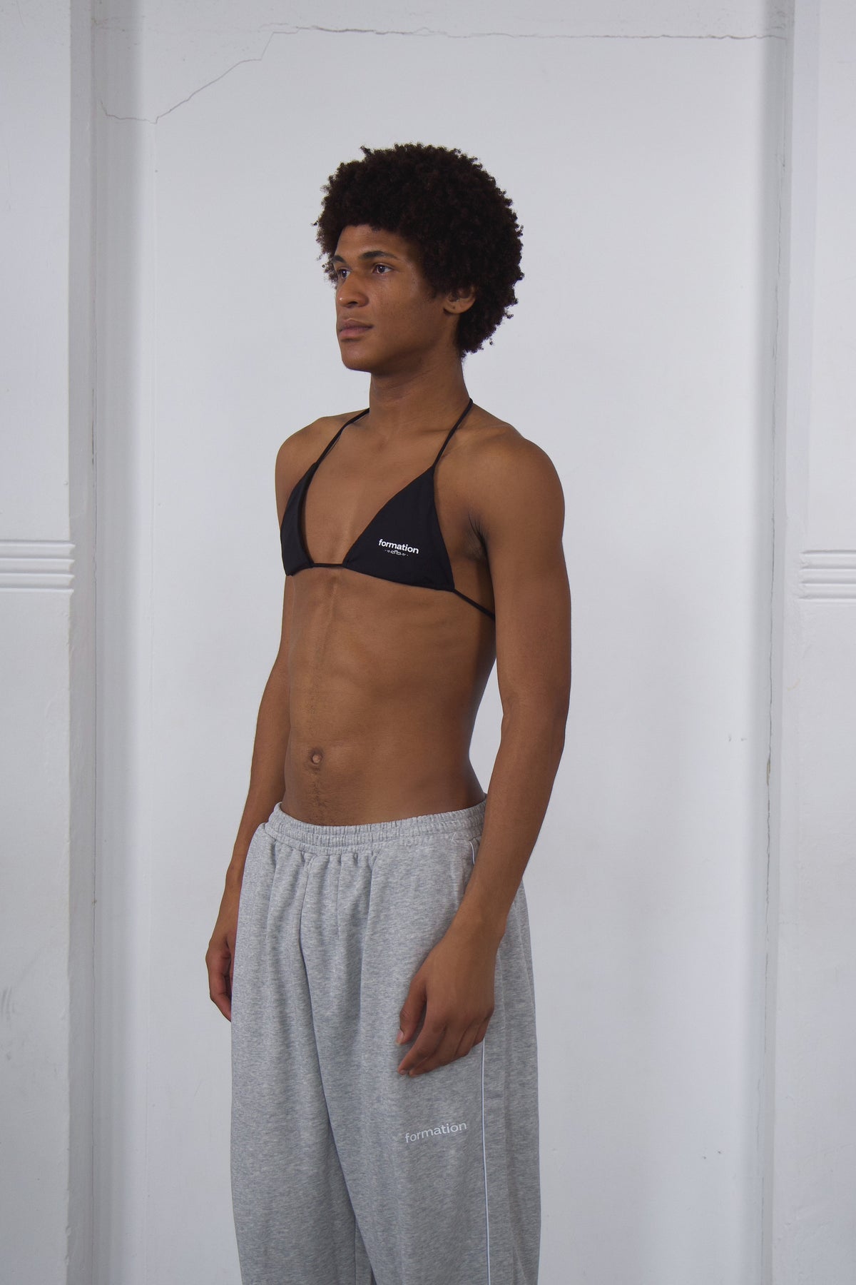 Person wearing a black bikini top and gray sweatpants against a white background