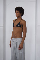 Person wearing a black bikini top and gray sweatpants against a white background