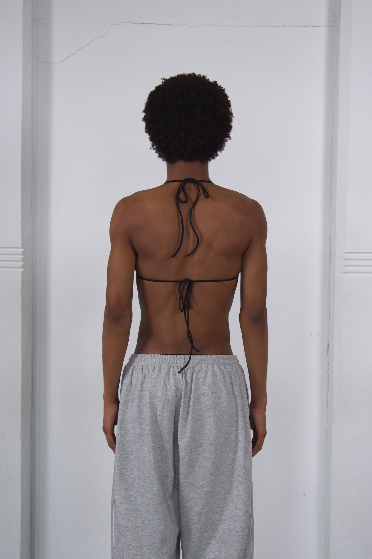 Person wearing a thin black bikini top with gray sweatpants against a white background