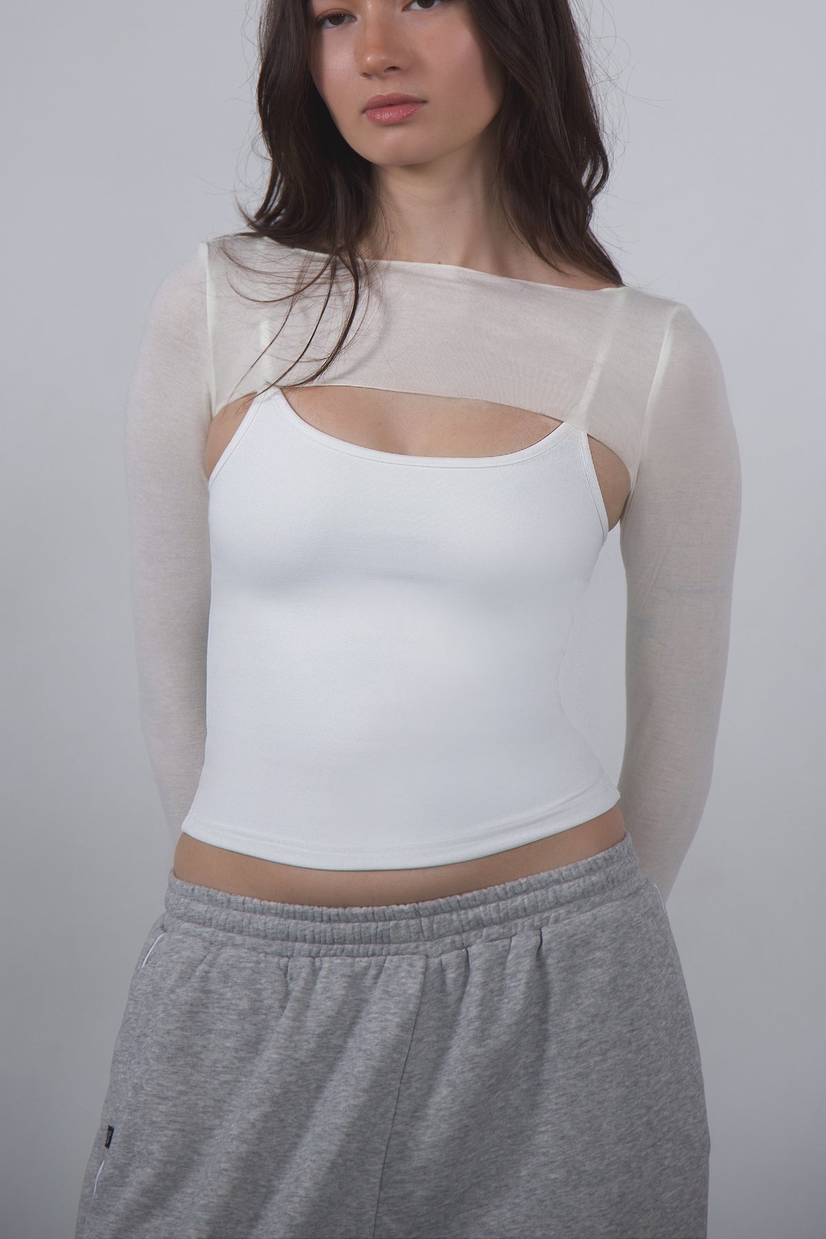 Woman wearing a white top with sheer sleeves and gray pants against a plain background